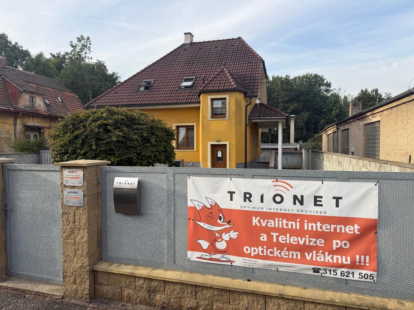 Kancelář TRIONETU v Kamenické ulici v Mělníku – žlutá budova, na plotě banner TRIONET